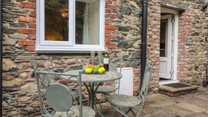 A stone cottage with a small table and chairs, a window, and a door. - Maple Cottage (Keswick)