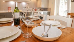 A dining table set with white plates, wine glasses, and a bottle of Rioja wine. - Maple Cottage (Keswick)