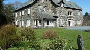 A large stone house with multiple windows and a well-maintained lawn. - Maple Cottage (Keswick)