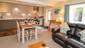 A modern kitchen with a dining area, a black leather sofa, and a view of the outdoors. - Maple Cottage (Keswick)