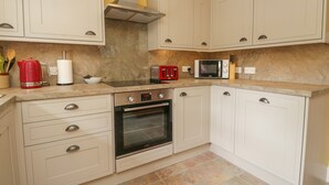A kitchen with white cabinets, a stove, a microwave, and a toaster. - Anvil Cottage (Ambleside)