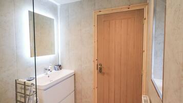 Een badkamer met een houten deur, een witte wastafel, een handdoekrek en een spiegel.