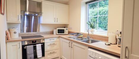 A compact kitchen with white cabinets, a stainless steel range, a microwave, a sink, and a built-in washing machine.