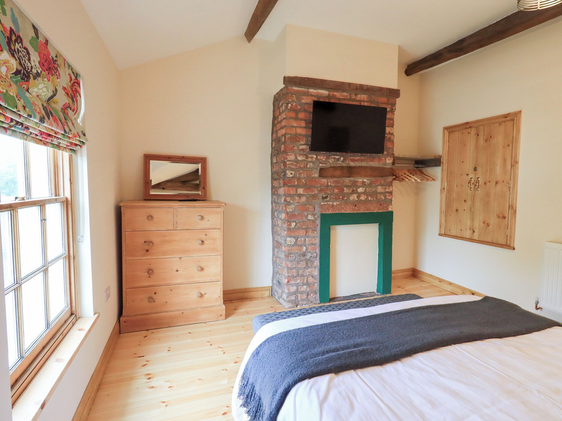 A bedroom with a wooden dresser, a brick fireplace, a bed with a blanket, and a window with curtains.