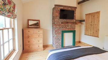 A bedroom with a wooden dresser, a brick fireplace, a bed with a blanket, and a window with curtains.