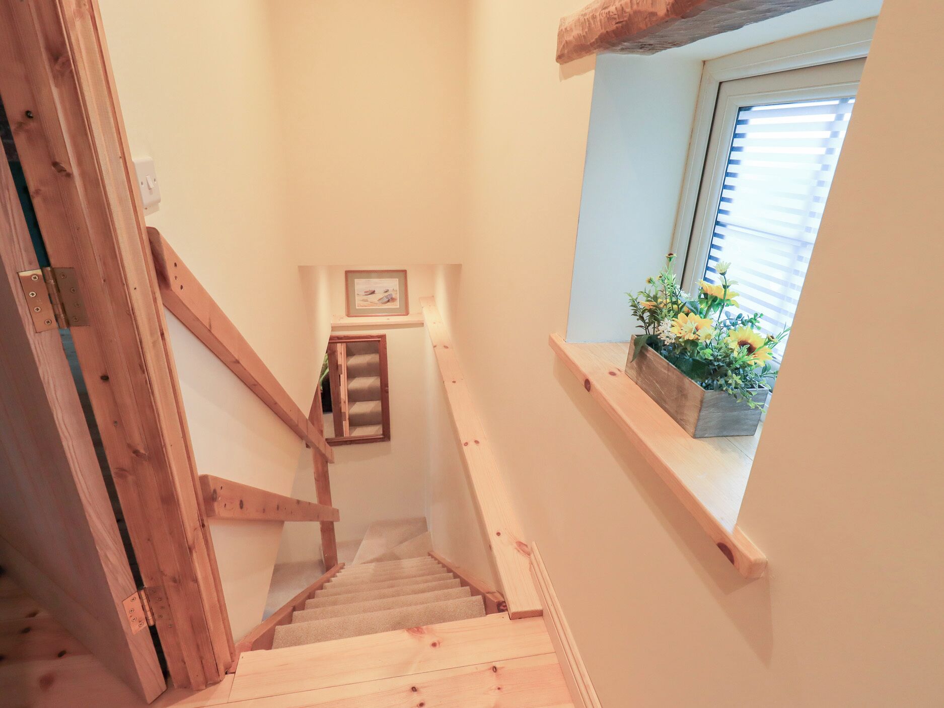 A wooden staircase with a handrail, a small window with a flower box, and a framed picture on the wall.