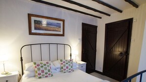 Un lit bien fait, avec du linge de lit blanc et des coussins à motifs, une table de chevet avec une lampe et un tableau encadré au mur.