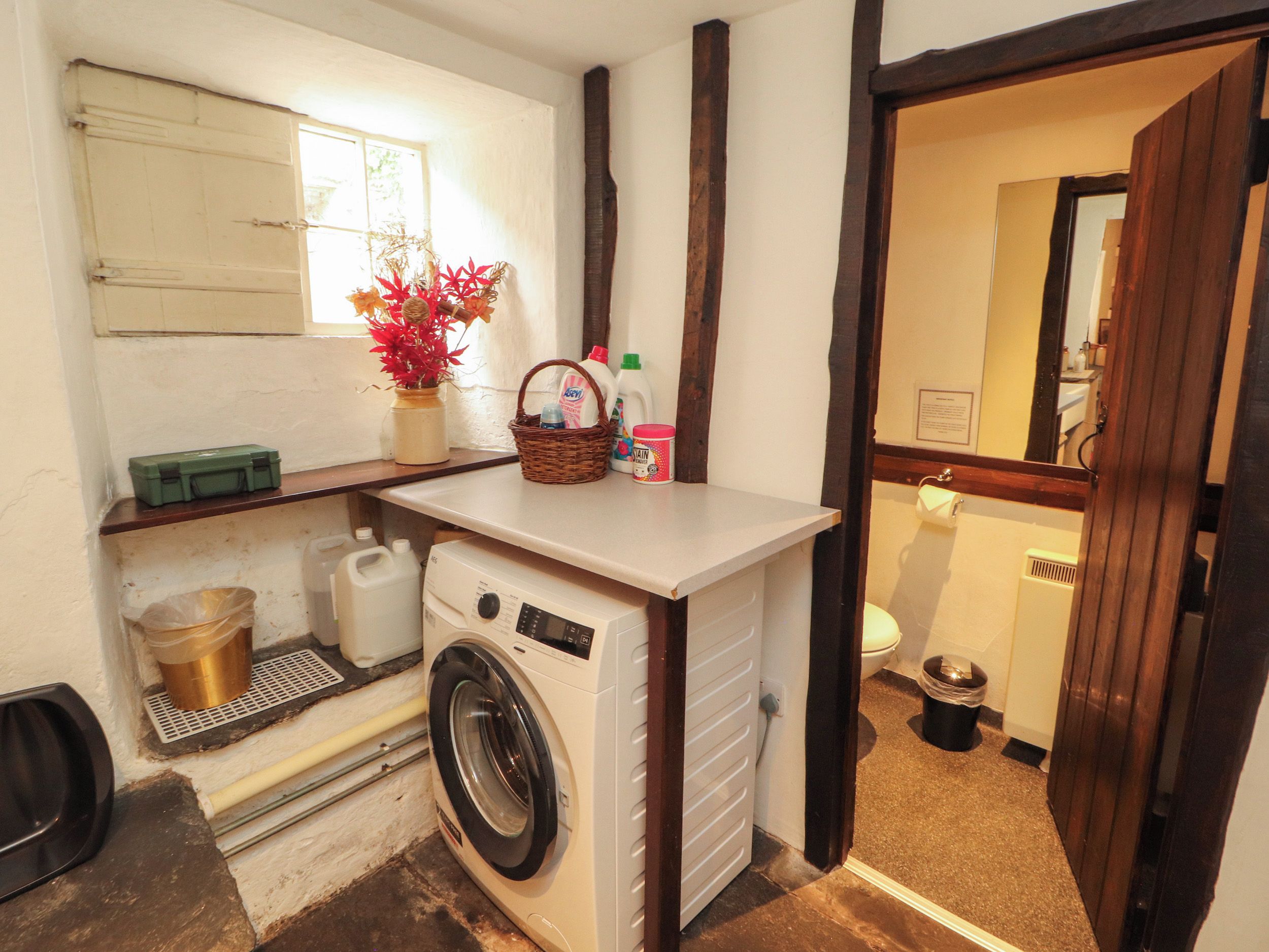 A compact laundry area with a washing machine, a shelf with a basket, and a window.
