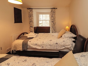 A bedroom with a bed, a bedside table, a lamp, a window with curtains, and a radiator.