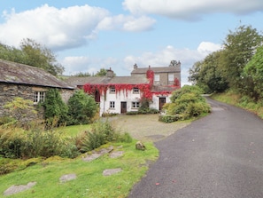 A stone cottage with ivy, a gravel path, and a narrow road.