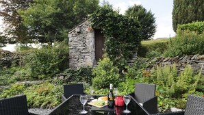 Een terras met eethoek, een stenen muur, weelderige beplanting en rieten meubels.