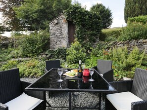 Un espace de restauration en plein air agrémenté d’un mur en pierre, d’une végétation luxuriante et de mobilier en osier.