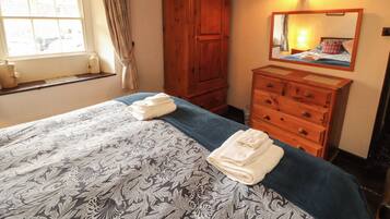 Un dormitorio con una cama, un aparador de madera, un espejo y una ventana con cortinas.