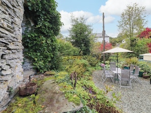 A garden with a stone wall, a metal chair, and a table under a canopy.