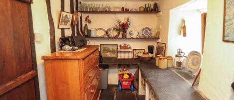 A kitchen with a wooden counter, a sink, and a stove. There are shelves with dishes and a trash bin.
