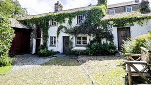 A traditional stone cottage with ivy-covered walls, a cobblestone courtyard, and a wooden bench. - Mill Cottage (Kendal)