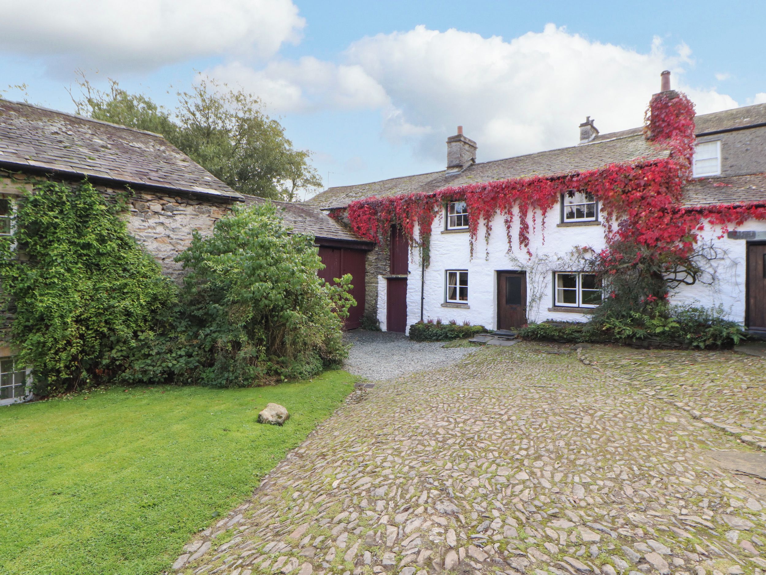 A traditional stone courtyard with a cobblestone path leading to a white building with red accents and ivy.