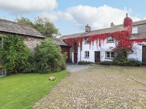 A traditional stone courtyard with a cobblestone path leading to a white building with red accents and ivy.