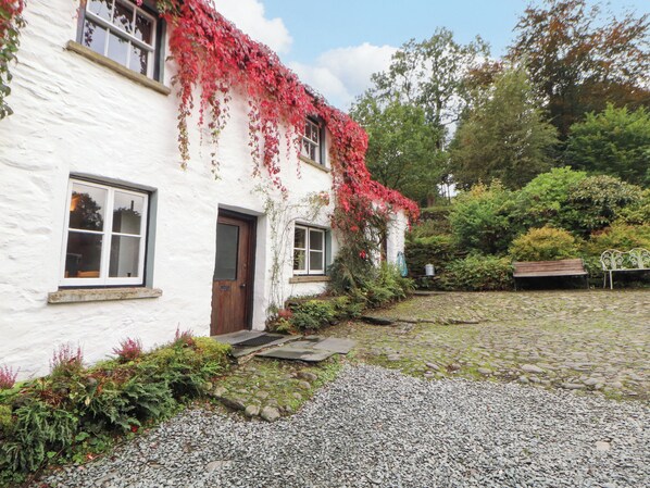 A white building with a cobblestone path leading to a wooden door. - Mill Cottage (Kendal)