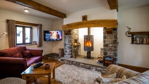 A cozy living room with a stone fireplace, a television mounted on the wall, and a comfortable seating area with a sofa and a chair. - Grayrigg Foot Stable (Kendal)