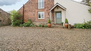 A two-story brick house with a white extension, a gravel driveway, and potted plants.