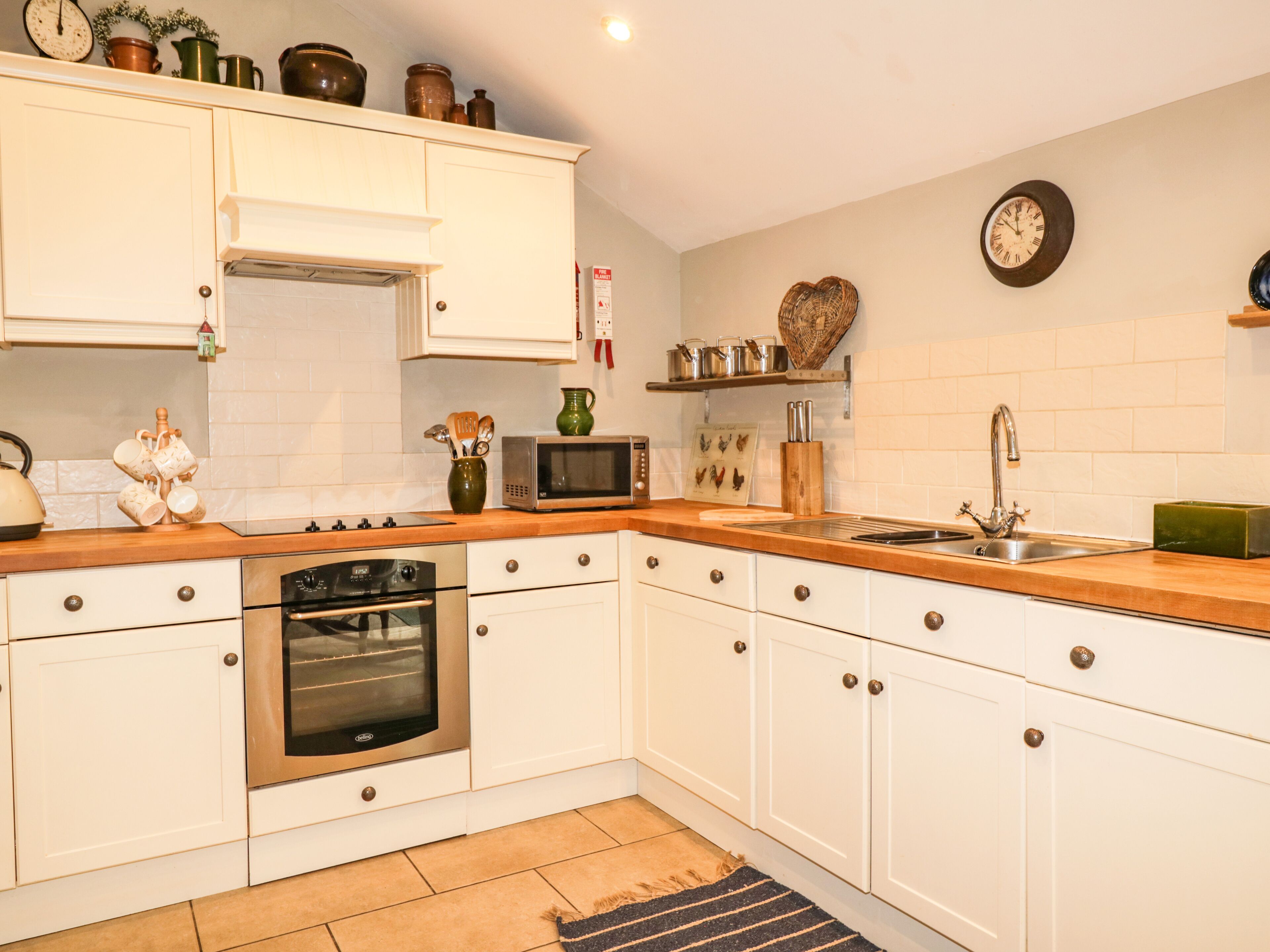 A kitchen with white cabinets, a microwave, an oven, a sink, and various kitchen utensils.