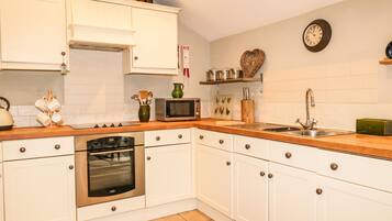 A kitchen with white cabinets, a microwave, an oven, a sink, and various kitchen utensils.
