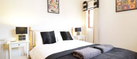 Une chambre à coucher bien rangée, avec un grand lit, deux tables de chevet, une commode et une fenêtre avec des rideaux.