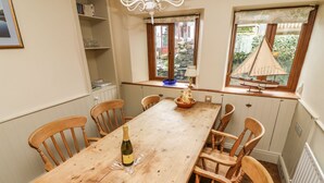 Un'area pranzo con un tavolo in legno, sei sedie in legno, una bottiglia di vino e una finestra che si affaccia su un giardino e una barca a vela.