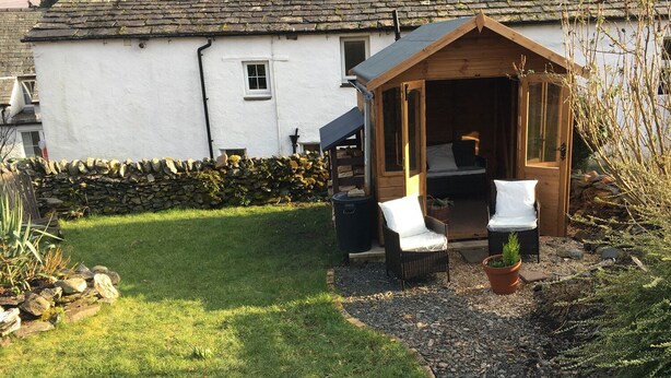 A cozy cottage with a small garden, a wooden porch, and a stone wall. - Nightingale Cottage (Keswick)