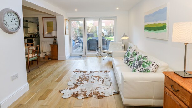 A modern living room with a white sofa, a cowhide rug, a dining area with wooden furniture, and a skylight. - Dovedale (Ryde)