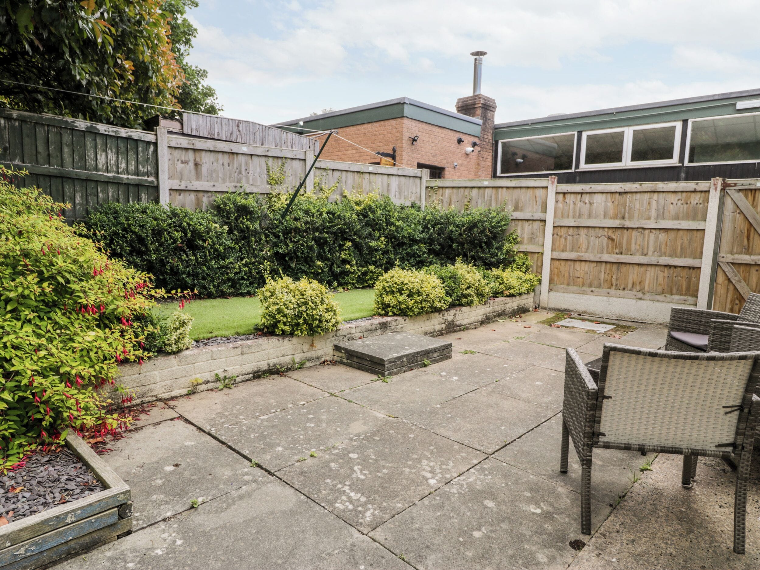 Un jardin avec une terrasse, une clôture en bois et un bâtiment en briques en arrière-plan.