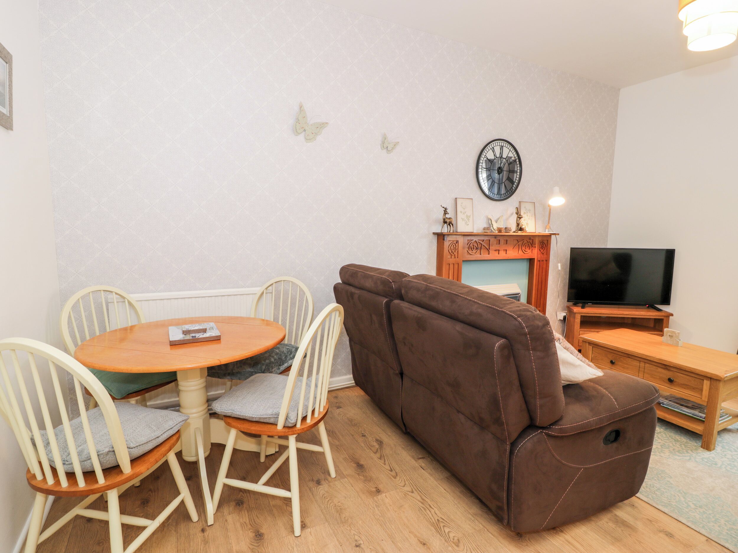 A living room with a brown sofa, a round wooden table with chairs, a fireplace, and a television.