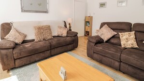 A living room with two brown leather sofas, a wooden coffee table, and a patterned rug. - Fairways (Prestatyn)