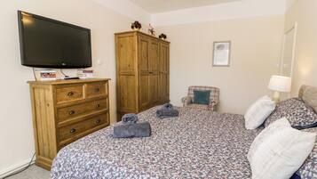 Une chambre à coucher comprenant un lit, une armoire en bois, une télévision, une chaise et une table de chevet avec une lampe.