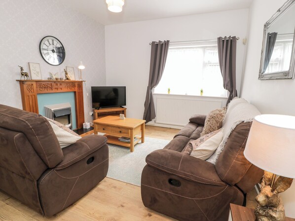 A living room with brown leather sofas, a wooden coffee table, a flat-screen TV, a fireplace, and a window with curtains. - Fairways (Prestatyn)
