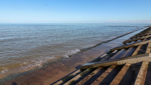 A coastal walkway with steps leading to the shore, a clear sky, and calm sea. - Fairways (Prestatyn)