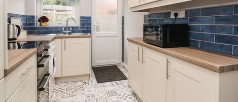 A kitchen with white cabinets, a black microwave, and patterned tile flooring.