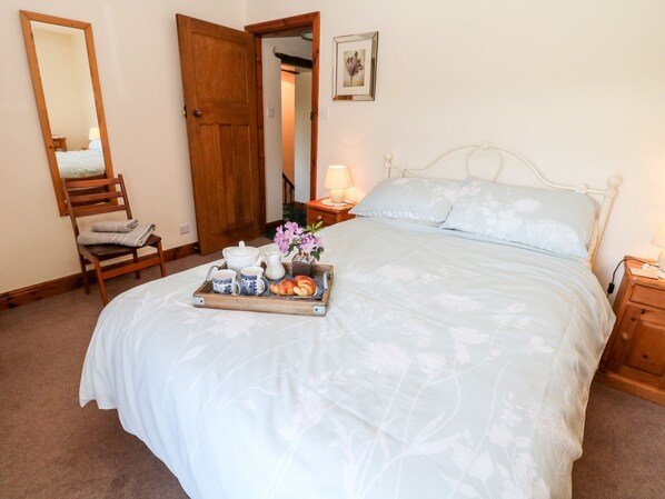 A bedroom with a large bed, a wooden chair, a tray with breakfast items, and a door leading to another room.