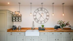 Une cuisine dotée d’une grande horloge murale, d’un plan de travail en bois et de meubles de couleur claire.
