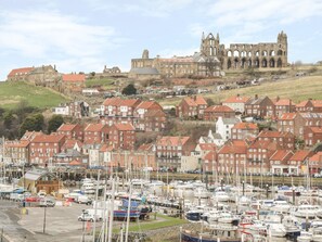 Uma vila costeira com um castelo histórico, edifícios residenciais e uma marina com barcos.