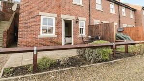 A two-story brick house with a front door, a small garden area with gravel and plants, and a wooden fence. - Platform 12 (Whitby)