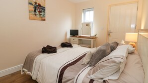 A bedroom with a bed, a desk, a television, and a painting on the wall. - Platform 12 (Whitby)