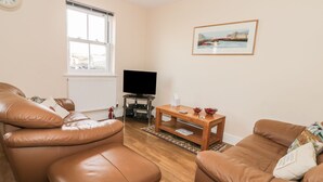 A living room with leather sofas, a wooden coffee table, a flat-screen TV, a window, and a framed picture on the wall. - Platform 12 (Whitby)