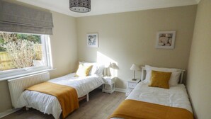 A bedroom with two beds, a window, and a radiator. - Oakdene (Milford Haven)