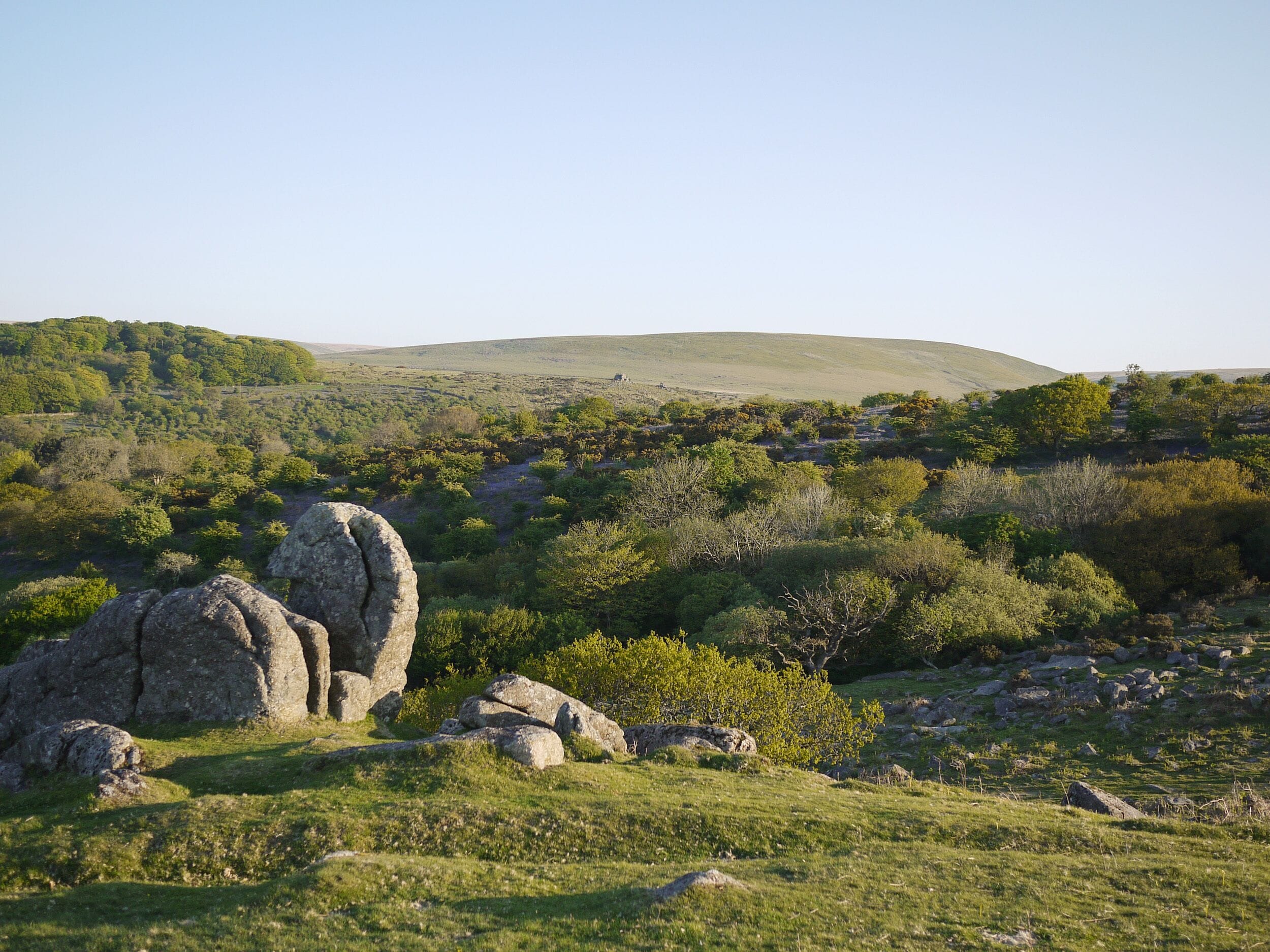 A natural landscape with rolling hills, dense greenery, and large boulders.