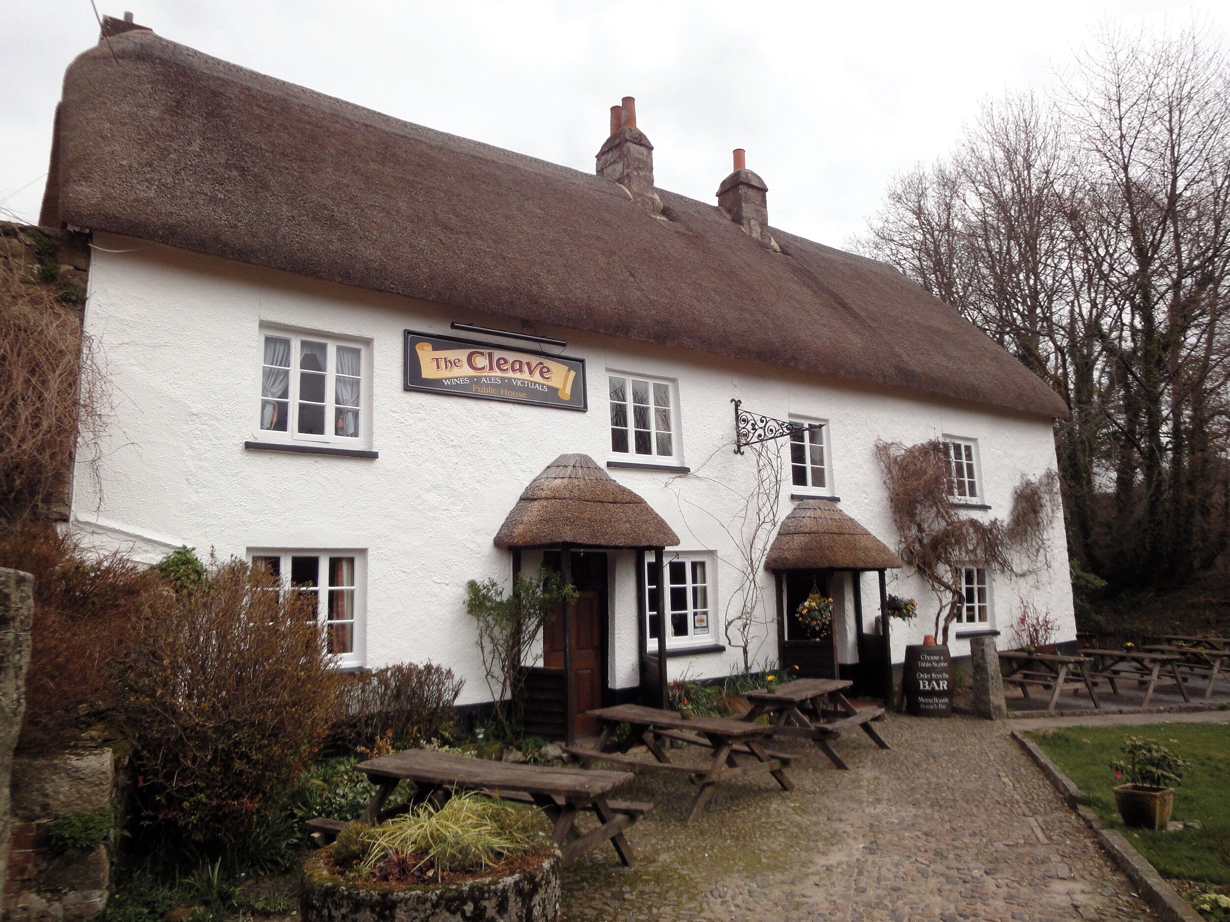 A traditional white building with a thatched roof, labeled "The Cleave," featuring multiple windows and a signboard.