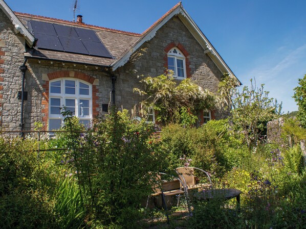 Een stenen huis met een schuin dak, zonnepanelen en een tuin met een houten bankje.