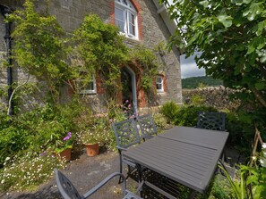 Een stenen huis met een tuin en een patio, een tafel en stoelen.