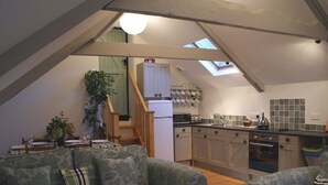 Un acogedor espacio habitable en el ático con comedor, kitchenette y una escalera que lleva a un dormitorio tipo loft.